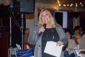 Colleen talking at the microphone in front of people sitting around tables