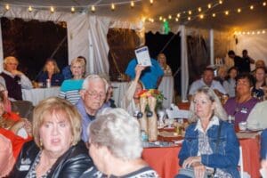 People sitting around tables, one of them has a paddle raised to bid at the auction