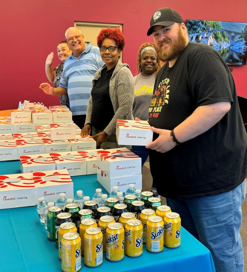 Group of staff standing by table with food and drinks
